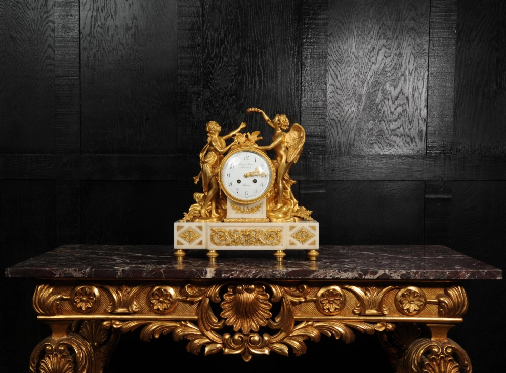 An antique French ormolu and white marble mantel clock featuring gilt bronze figures of Cupid and Psyche surrounding a central white enamel dial on a rectangular marble base. View III