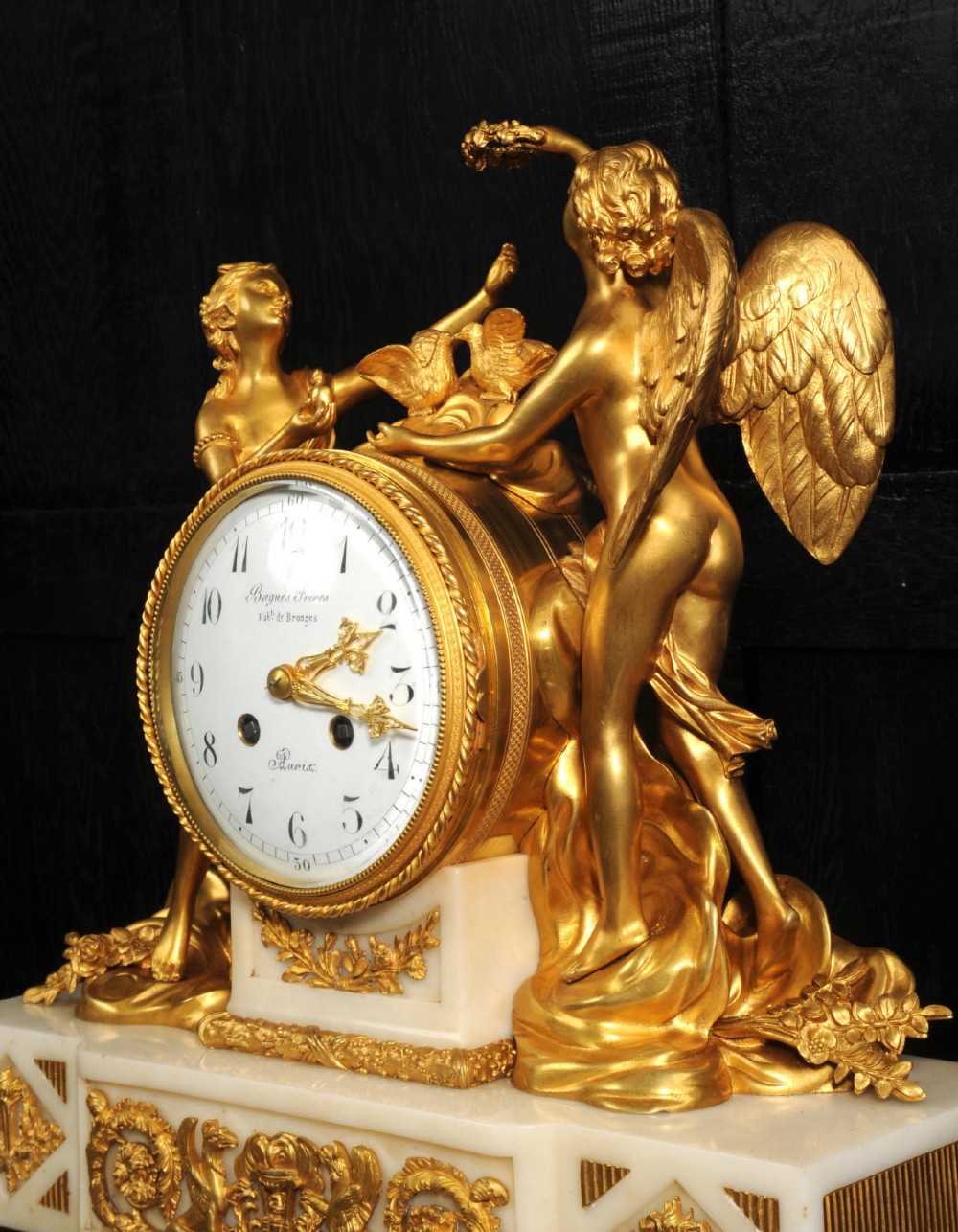 An antique French ormolu and white marble mantel clock featuring gilt bronze figures of Cupid and Psyche surrounding a central white enamel dial on a rectangular marble base. View IV