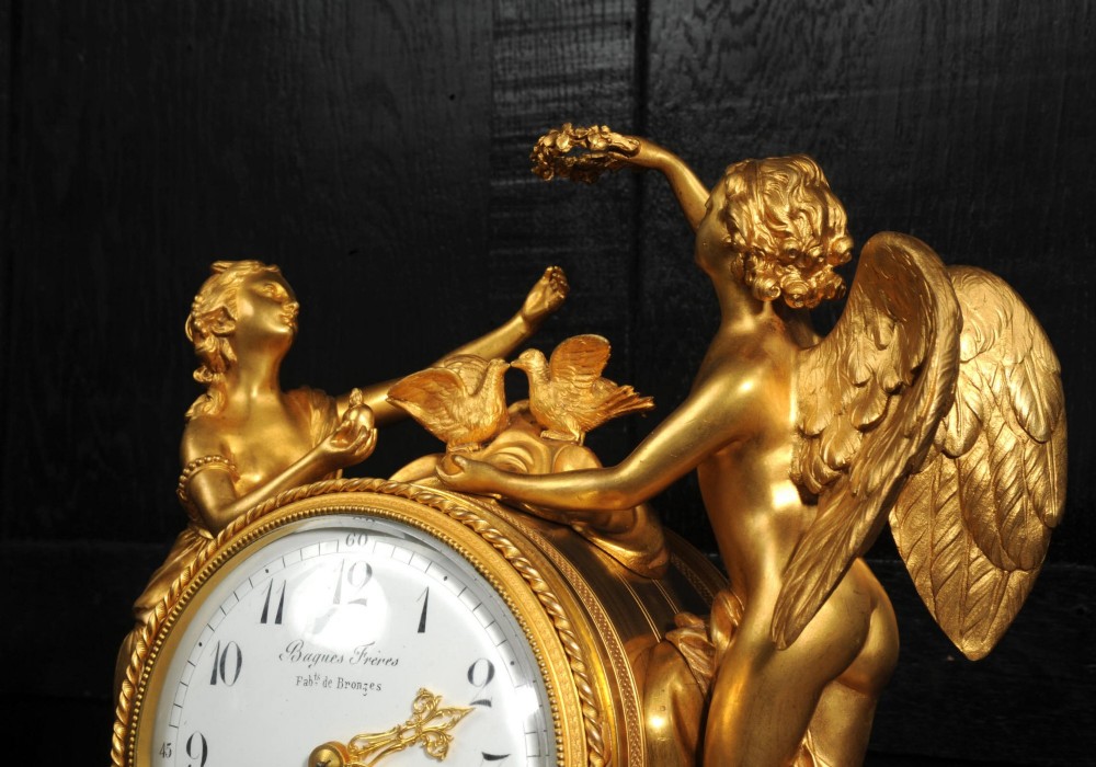 An antique French ormolu and white marble mantel clock featuring gilt bronze figures of Cupid and Psyche surrounding a central white enamel dial on a rectangular marble base. View V