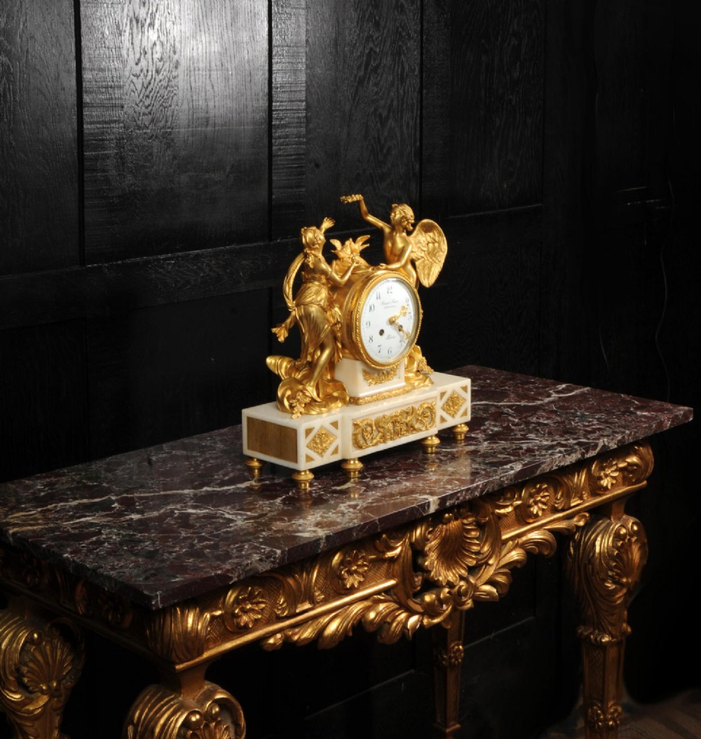 An antique French ormolu and white marble mantel clock featuring gilt bronze figures of Cupid and Psyche surrounding a central white enamel dial on a rectangular marble base. View VII