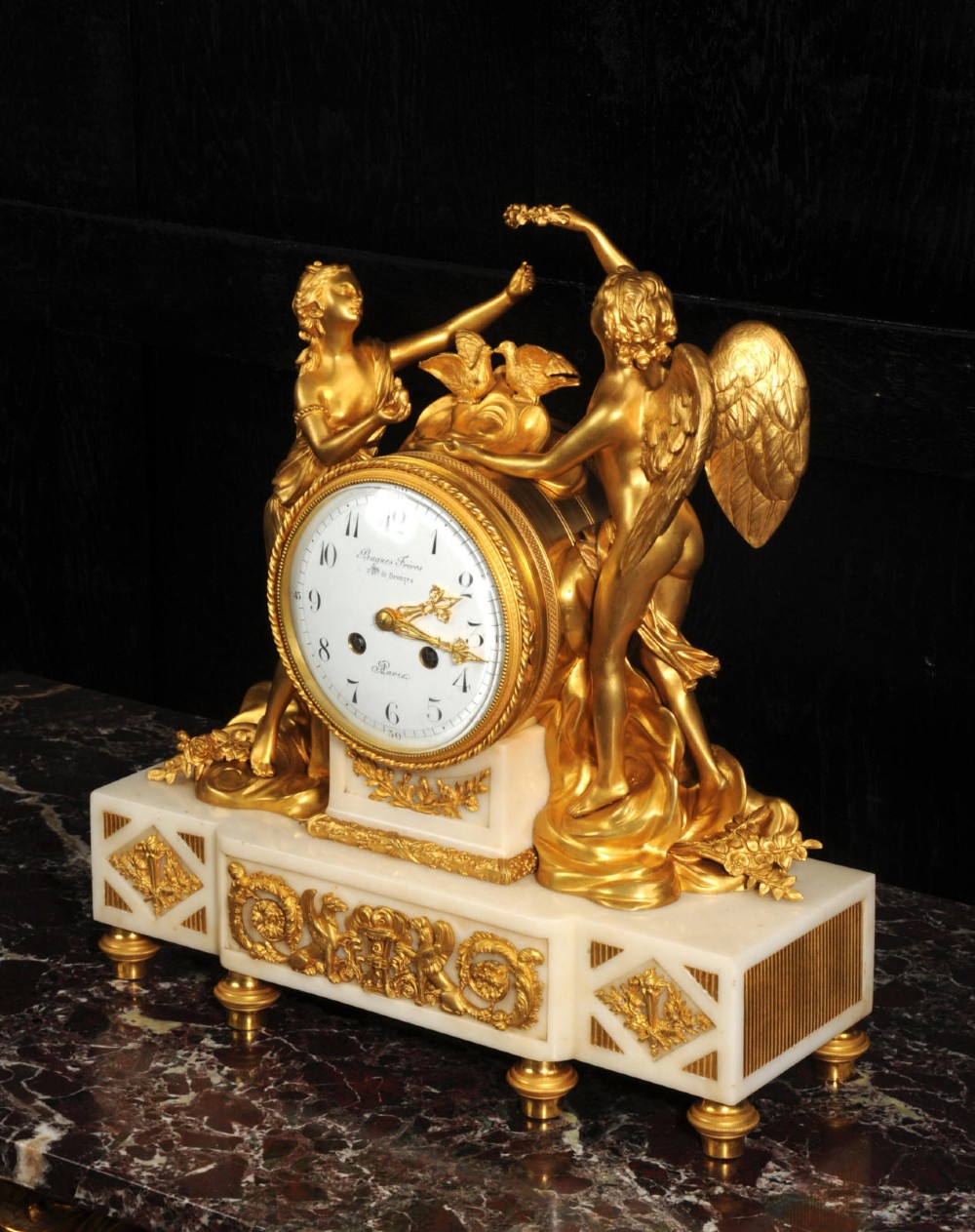 An antique French ormolu and white marble mantel clock featuring gilt bronze figures of Cupid and Psyche surrounding a central white enamel dial on a rectangular marble base. View VIII