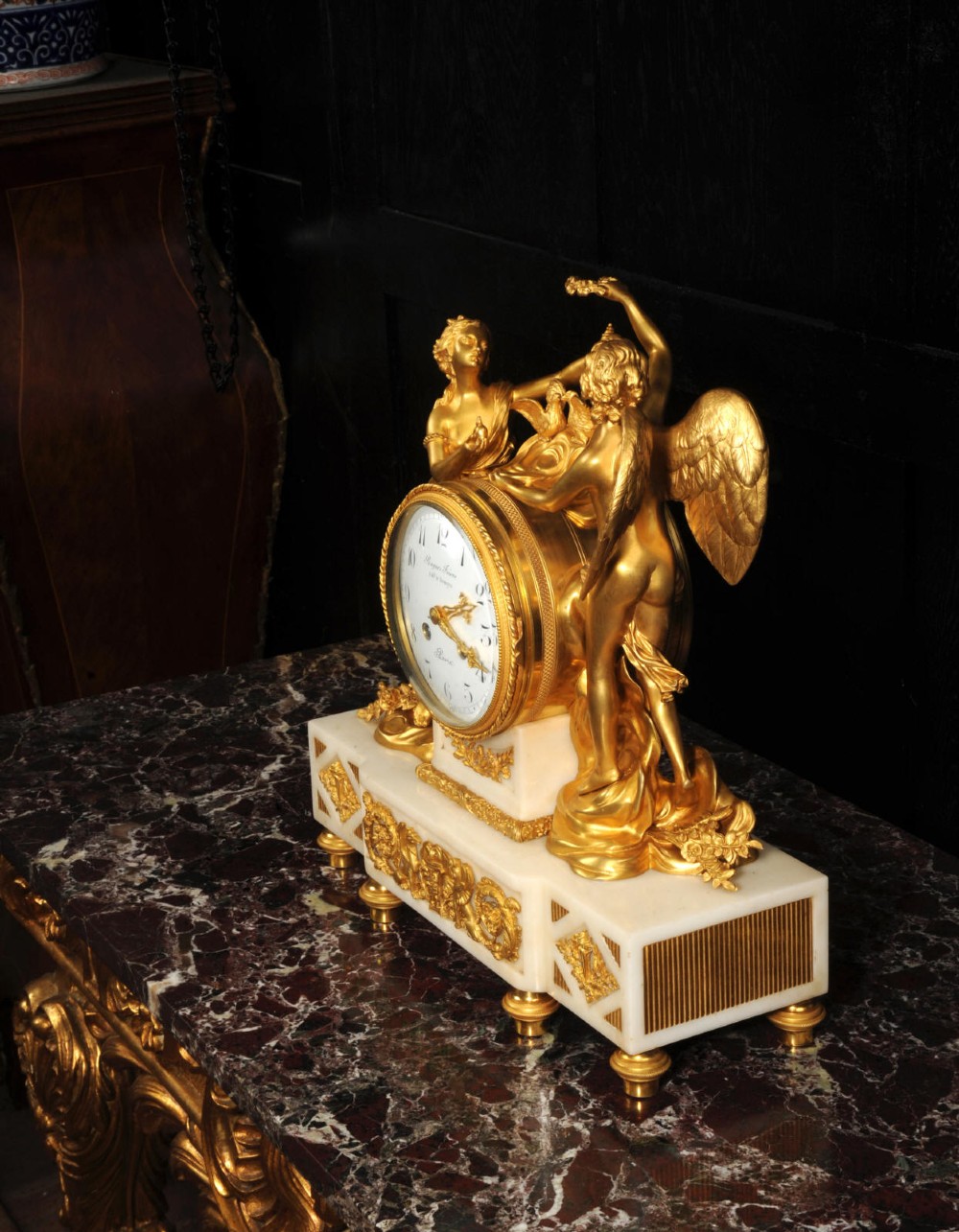 An antique French ormolu and white marble mantel clock featuring gilt bronze figures of Cupid and Psyche surrounding a central white enamel dial on a rectangular marble base. View IX
