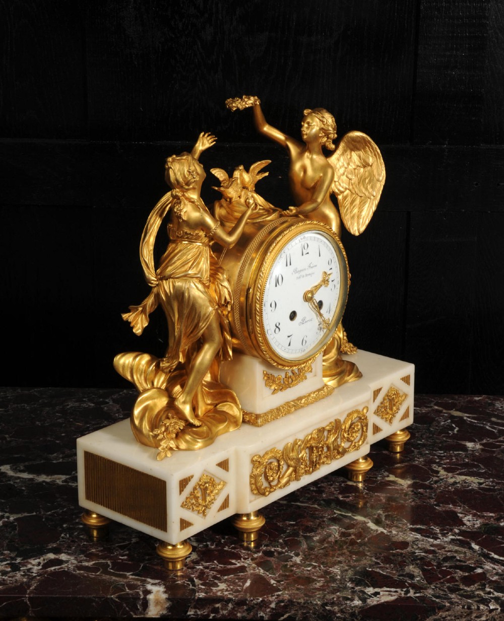 An antique French ormolu and white marble mantel clock featuring gilt bronze figures of Cupid and Psyche surrounding a central white enamel dial on a rectangular marble base. View X