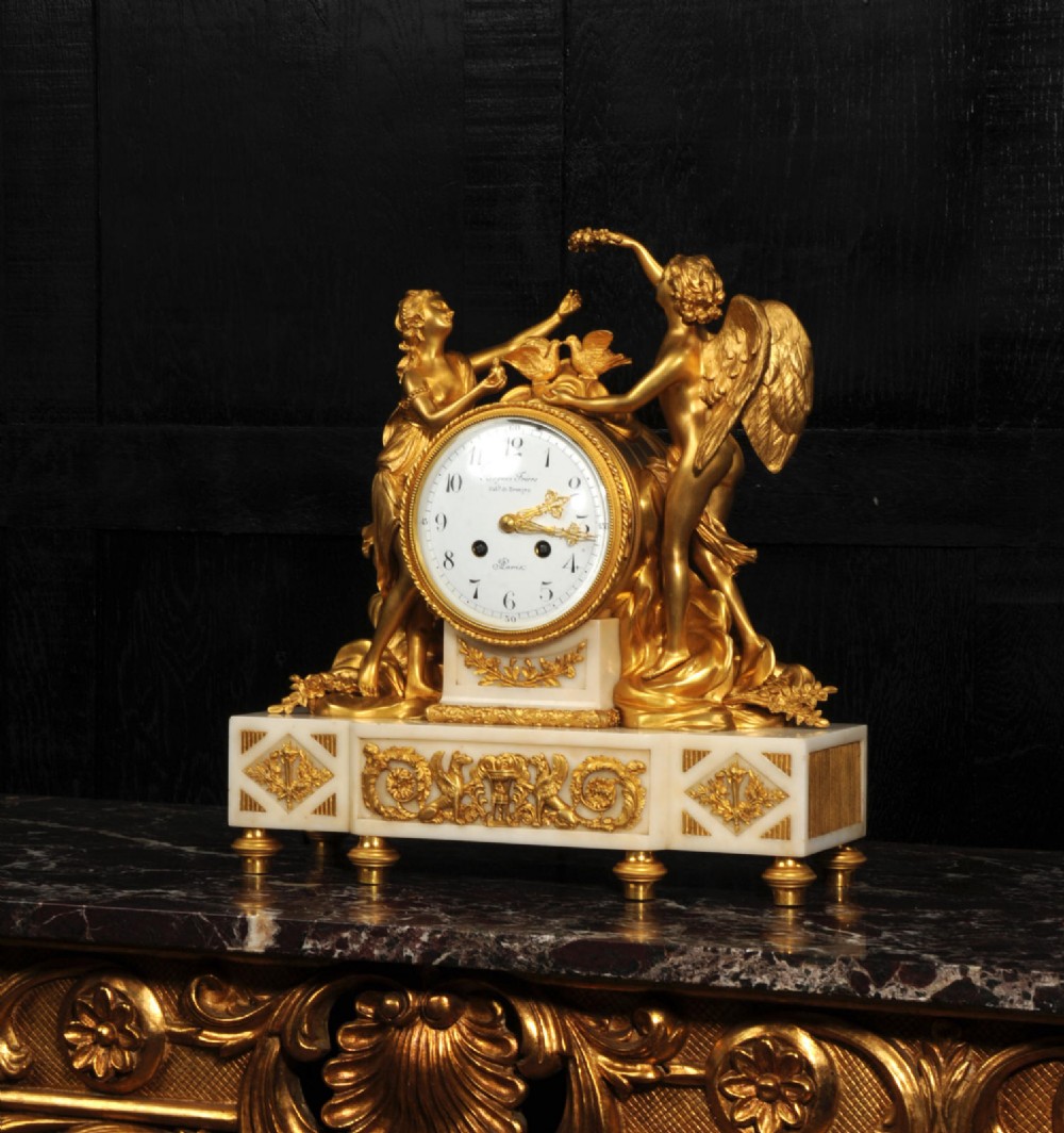 An antique French ormolu and white marble mantel clock featuring gilt bronze figures of Cupid and Psyche surrounding a central white enamel dial on a rectangular marble base. View XI