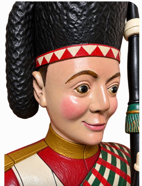 A nineteenth-century polychrome carved wooden figure of a Highland bagpiper in traditional dress seated on a wooden barrel. View II