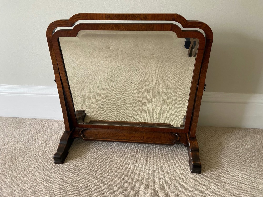 An Art Deco burr walnut dressing table mirror featuring a stepped arch frame set on a wooden swivel base with dual feet.