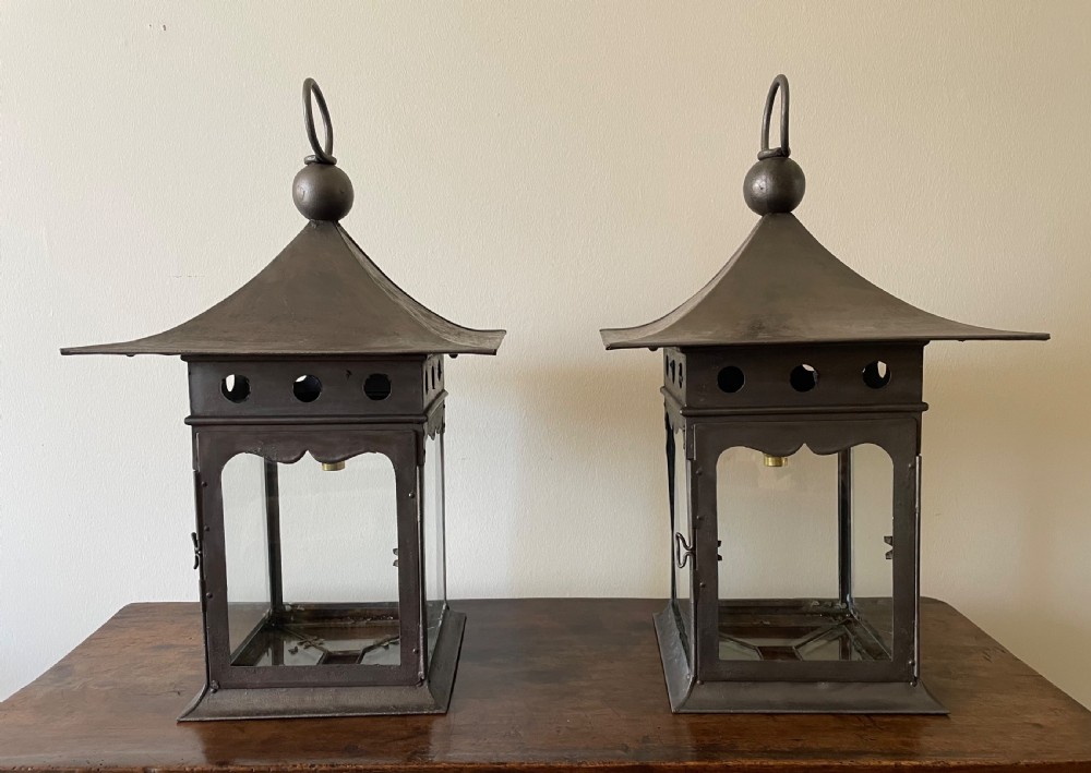 A pair of patinated dark iron Arts and Crafts lanterns featuring pagoda-style roofs, loop finials, circular pierced vents, and clear glass panels.
