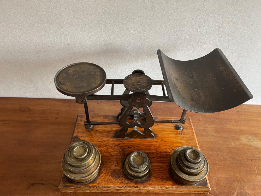 A set of Victorian brass postal scales mounted on a rectangular wooden base with nested brass weights stored in custom cutouts.