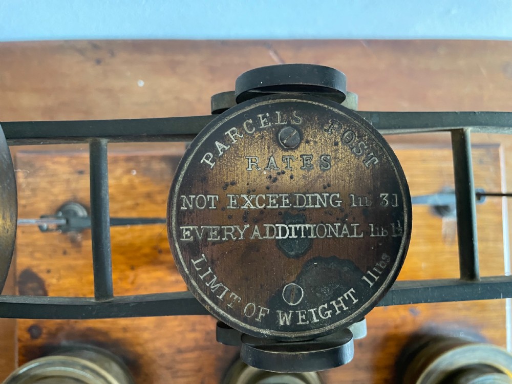 A set of Victorian brass postal scales mounted on a rectangular wooden base with nested brass weights stored in custom cutouts. View V