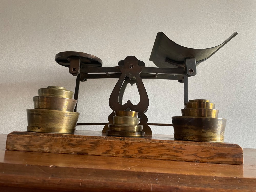 A set of Victorian brass postal scales mounted on a rectangular wooden base with nested brass weights stored in custom cutouts. View VII
