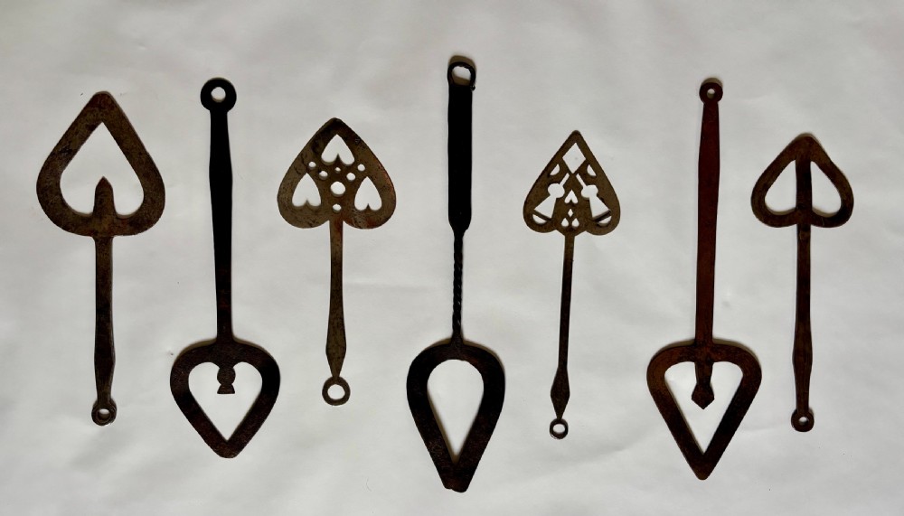 A set of seven hand-forged dark wrought iron Scottish bannock turners with decorative heart-shaped pierced blades and elongated handles.