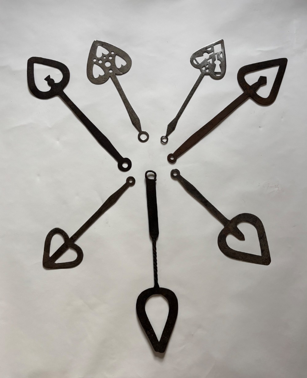 A set of seven hand-forged dark wrought iron Scottish bannock turners with decorative heart-shaped pierced blades and elongated handles. View II