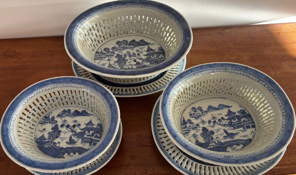 A set of three Chinese export blue and white porcelain reticulated baskets resting on matching pierced undertrays with hand-painted river landscape scenes.