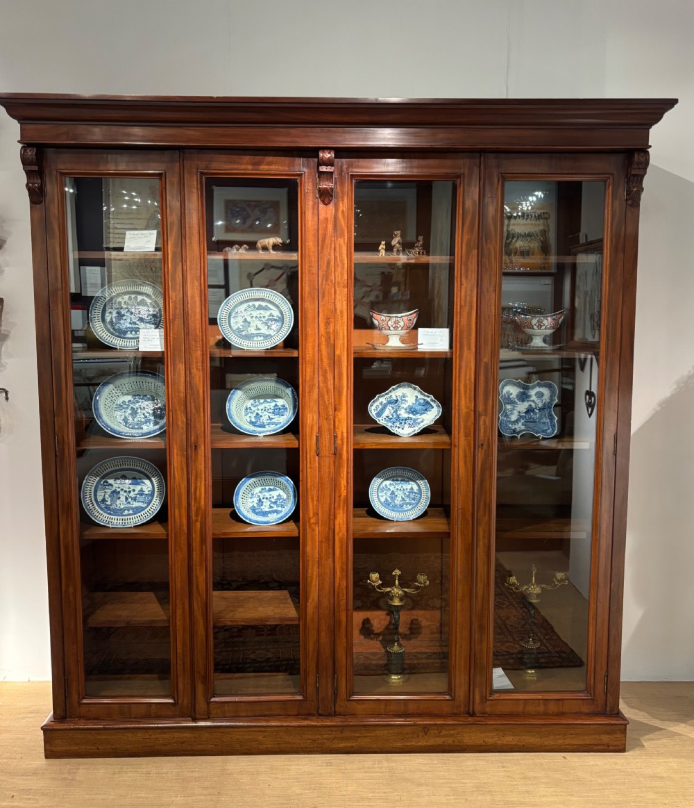 A large Mid-Victorian mahogany bookcase featuring four glazed doors, carved corbels at the upper corners, and adjustable internal shelving.