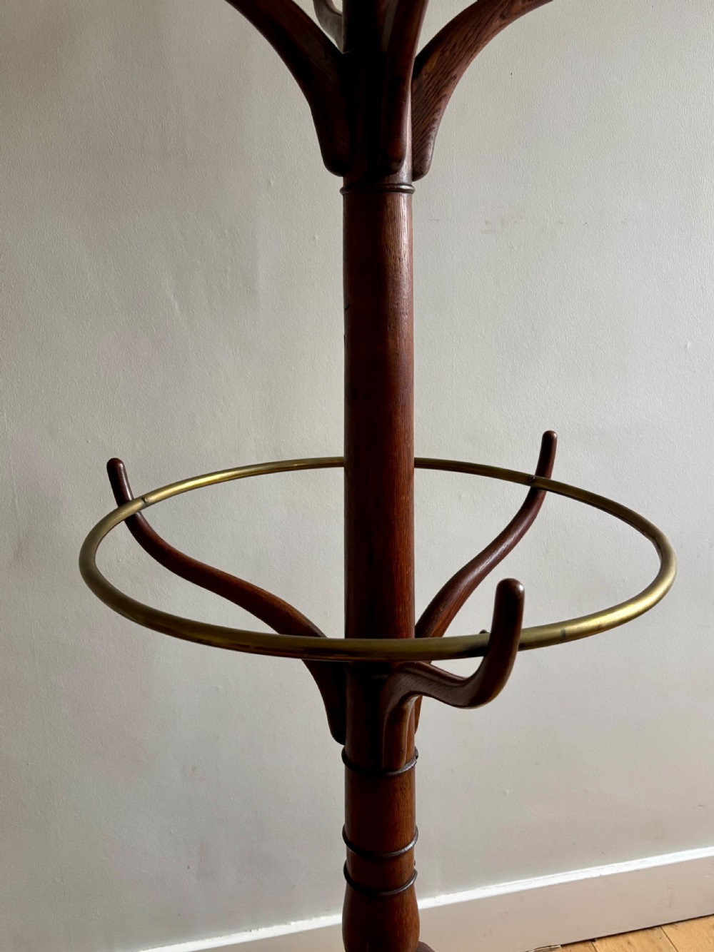 A dark oak Regency coat stand featuring multiple carved hooks, a central turned post, a circular brass umbrella ring, and splayed legs over a rounded drip tray. View III