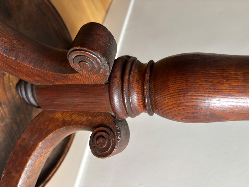A dark oak Regency coat stand featuring multiple carved hooks, a central turned post, a circular brass umbrella ring, and splayed legs over a rounded drip tray. View IV