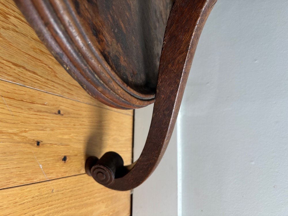 A dark oak Regency coat stand featuring multiple carved hooks, a central turned post, a circular brass umbrella ring, and splayed legs over a rounded drip tray. View V