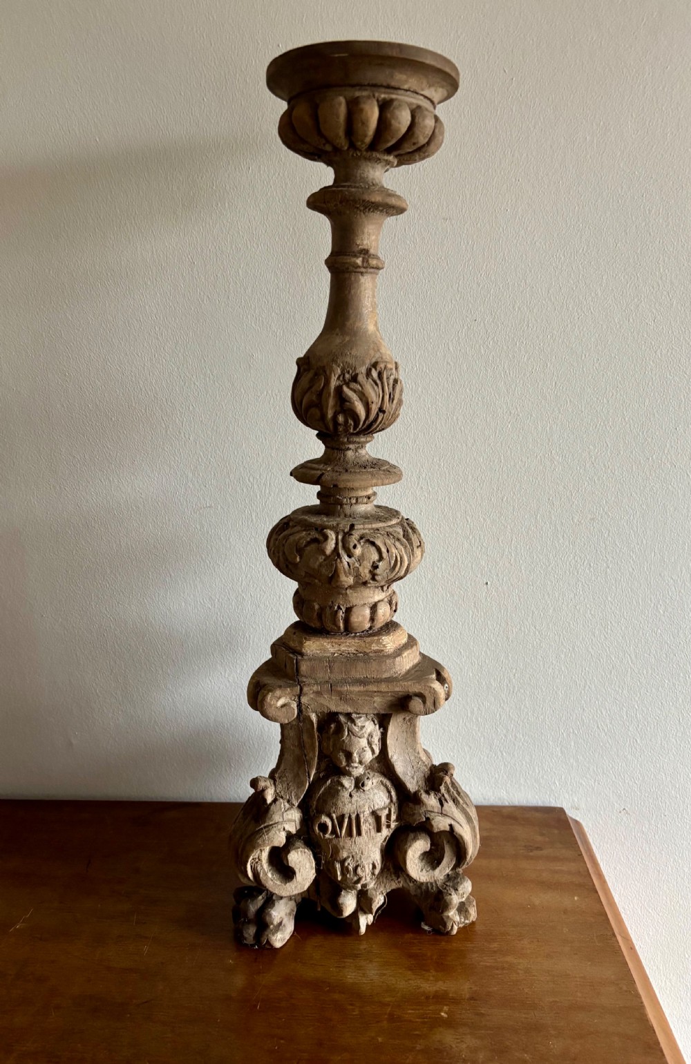 A tall 17th-century carved limewood candlestick featuring a scrollwork base with a carved cherub face, gadrooned stem, and dripan top.