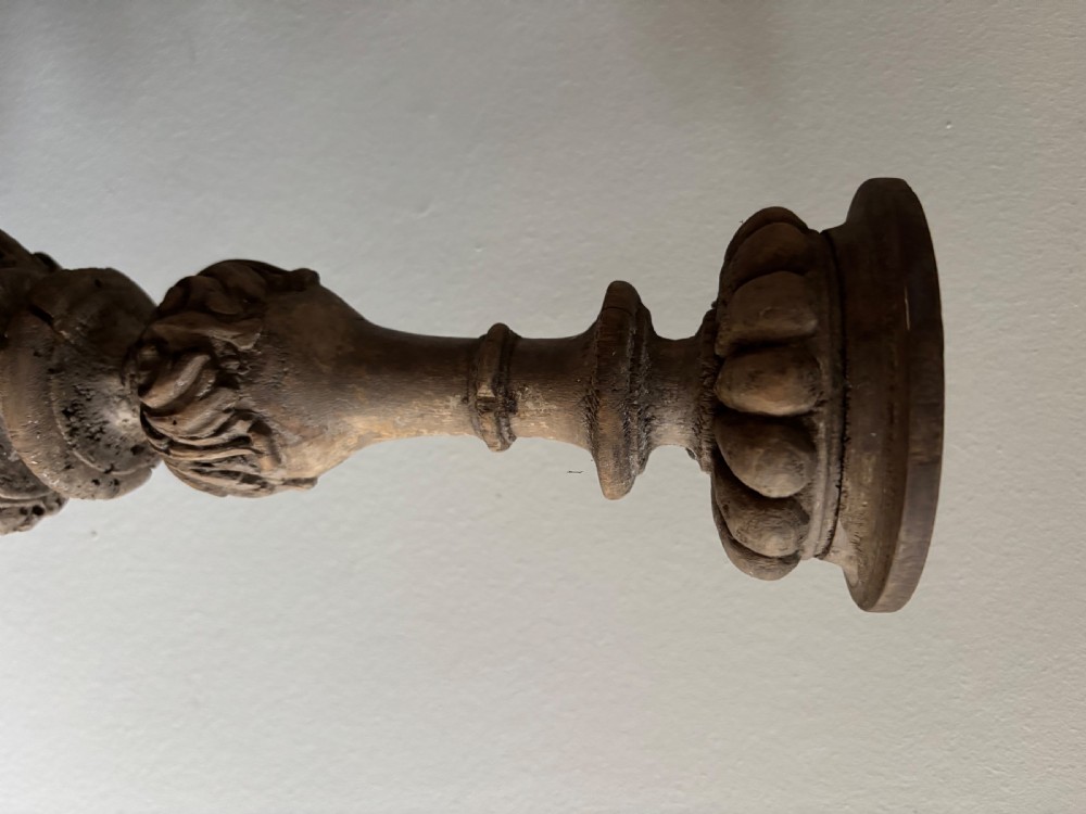 A tall 17th-century carved limewood candlestick featuring a scrollwork base with a carved cherub face, gadrooned stem, and dripan top. View IV