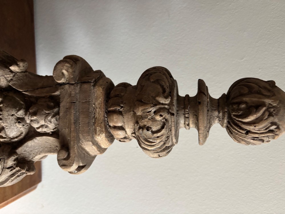A tall 17th-century carved limewood candlestick featuring a scrollwork base with a carved cherub face, gadrooned stem, and dripan top. View V