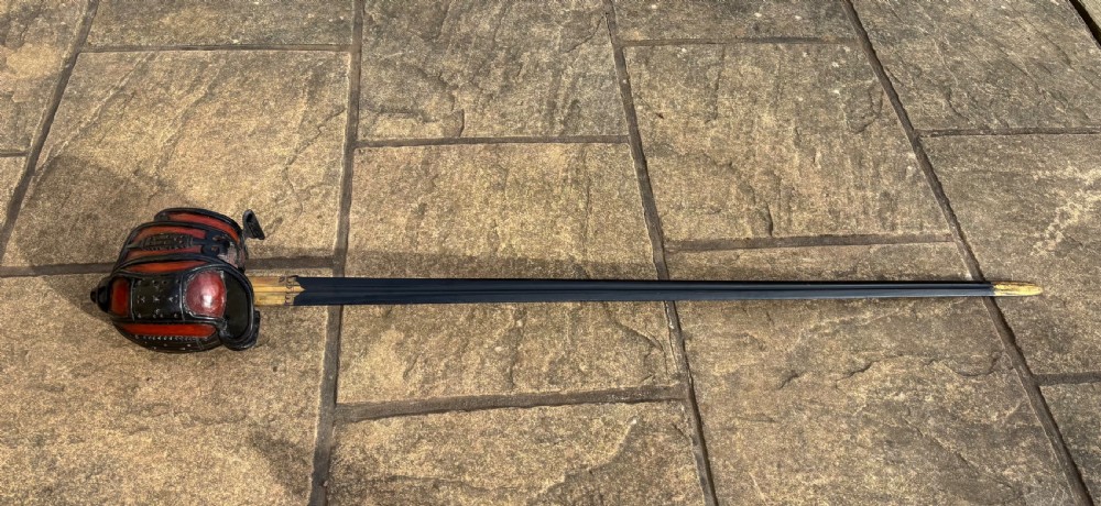 A Scottish wooden broadsword featuring a long dark blade and a basket guard lined with red leather.