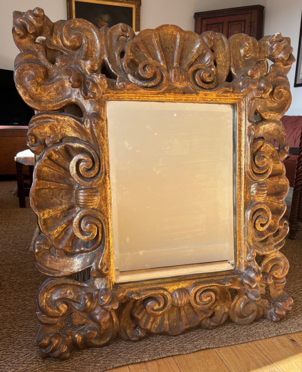 A rectangular mirror enclosed within a heavily carved giltwood frame featuring elaborate scrollwork and shell motifs.