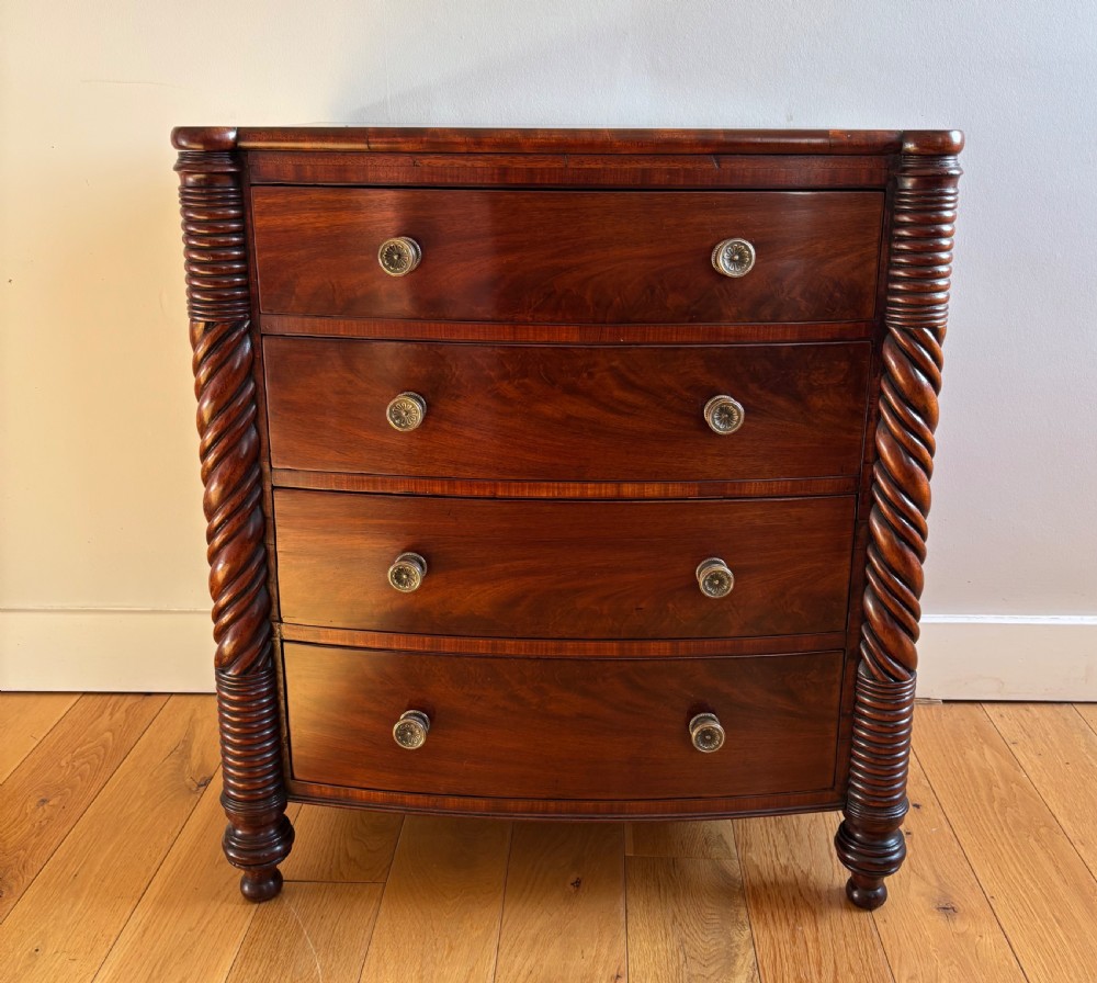 A small William IV mahogany bowfront chest of four drawers flanked by carved spiral-twist side columns and supported on turned feet.