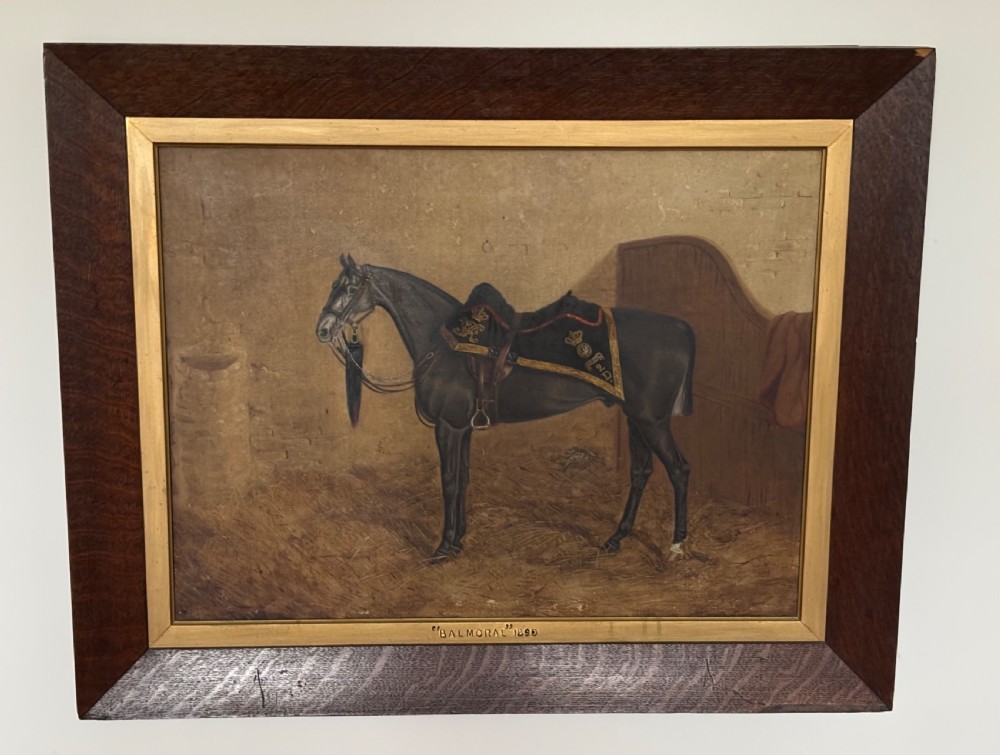 A late Victorian equestrian oil painting depicting a dark horse titled Balmoral in a stable setting, presented within a wide oak frame with a gilt inner slip.
