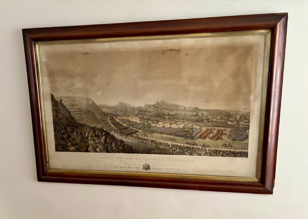 A framed Victorian military print depicting a panoramic view of the Royal Review of the Scottish Volunteers in a dark wooden frame with a gold slip.
