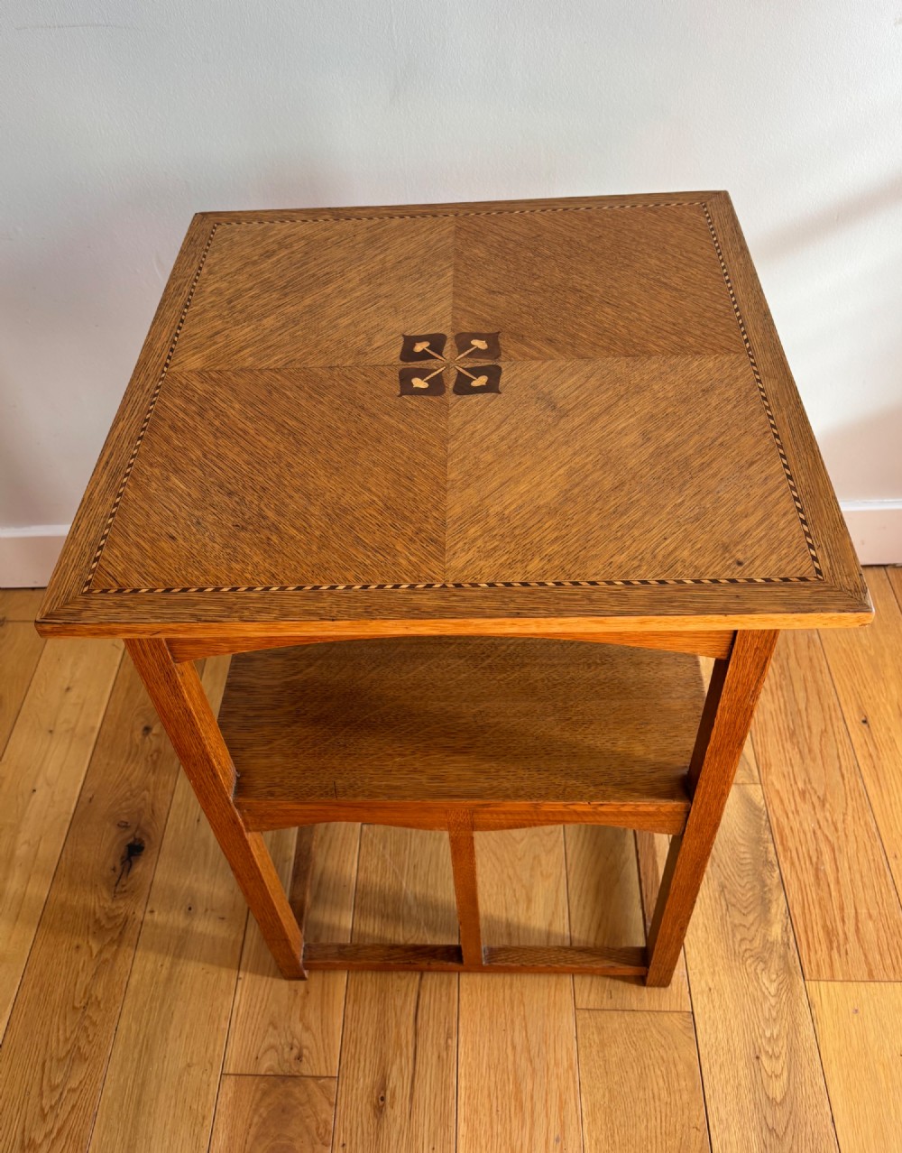 An antique Arts and Crafts square oak occasional table featuring a central marquetry motif, banded inlay border, lower tier shelf, and straight legs. View V