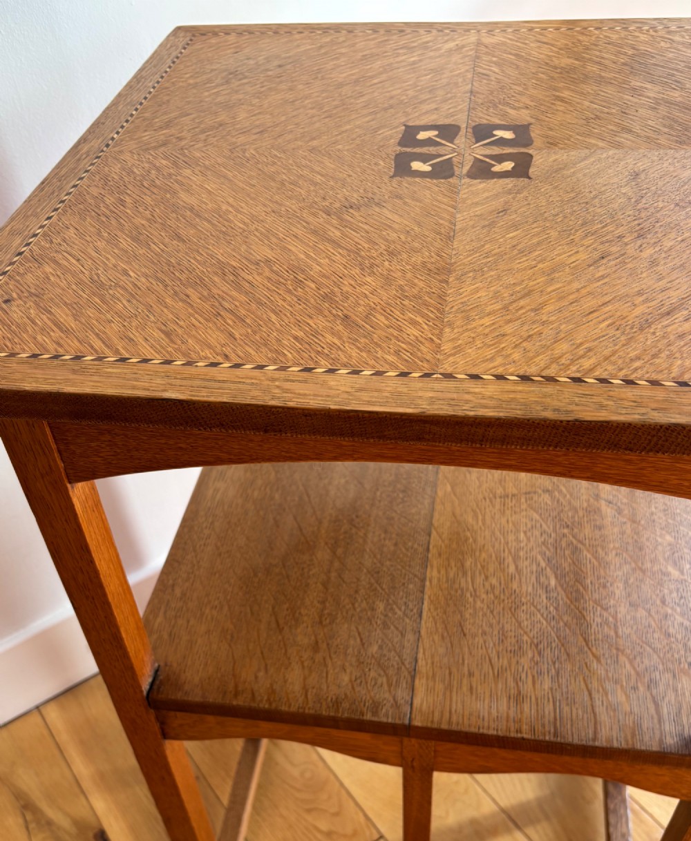 An antique Arts and Crafts square oak occasional table featuring a central marquetry motif, banded inlay border, lower tier shelf, and straight legs. View VII