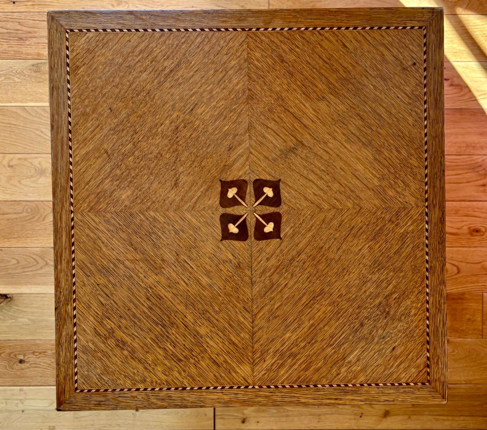 An antique Arts and Crafts square oak occasional table featuring a central marquetry motif, banded inlay border, lower tier shelf, and straight legs. View VIII