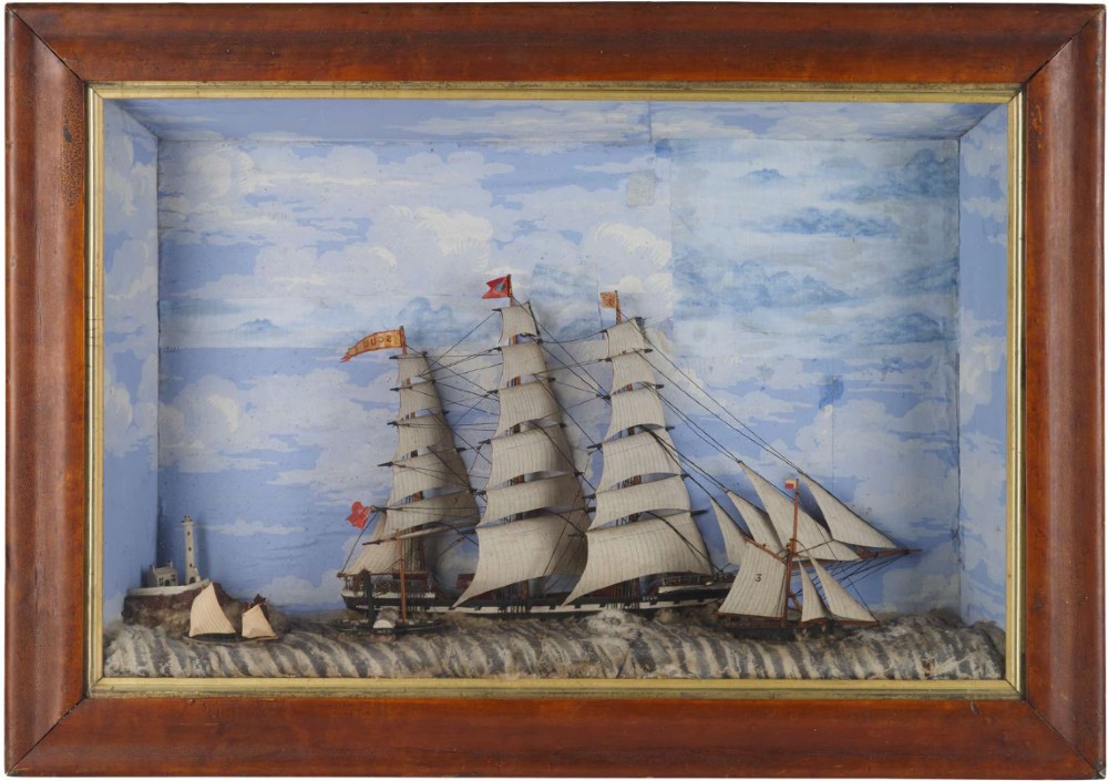 A Victorian glazed shadow box diorama depicting a three-masted clipper ship in full sail alongside a smaller vessel and lighthouse, framed in a polished wooden frame with a gilt slip.