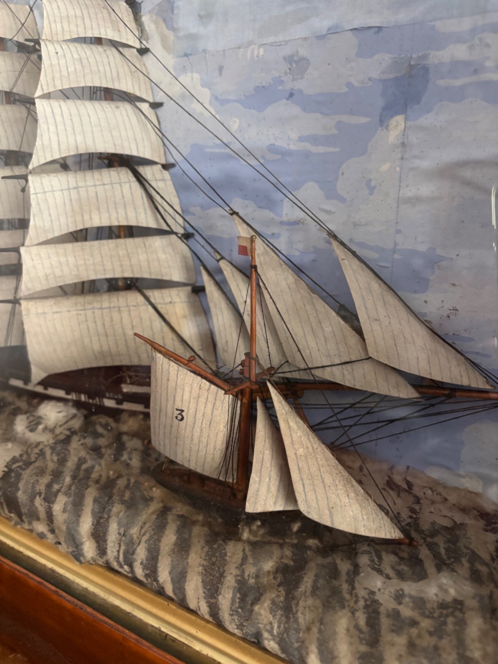 A Victorian glazed shadow box diorama depicting a three-masted clipper ship in full sail alongside a smaller vessel and lighthouse, framed in a polished wooden frame with a gilt slip. View IV