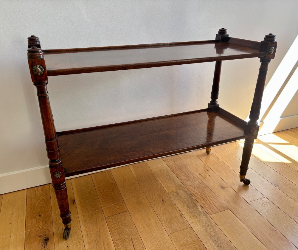 A two-tier mahogany Regency whatnot featuring turned upright supports, carved rosette details on corner blocks, top finials, and brass castors.