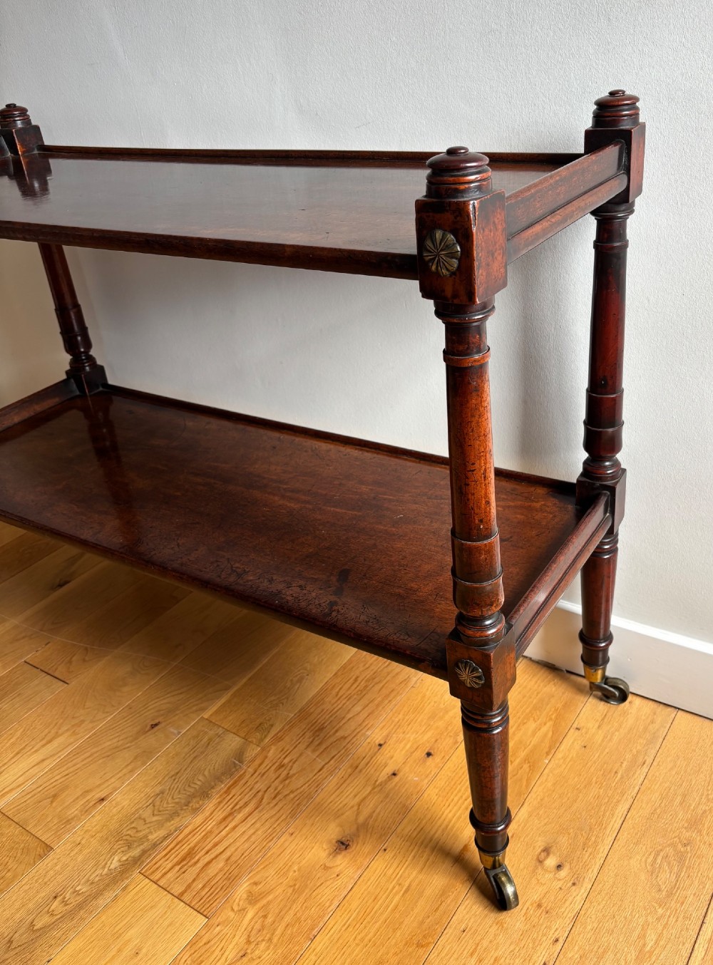 A two-tier mahogany Regency whatnot featuring turned upright supports, carved rosette details on corner blocks, top finials, and brass castors. View III