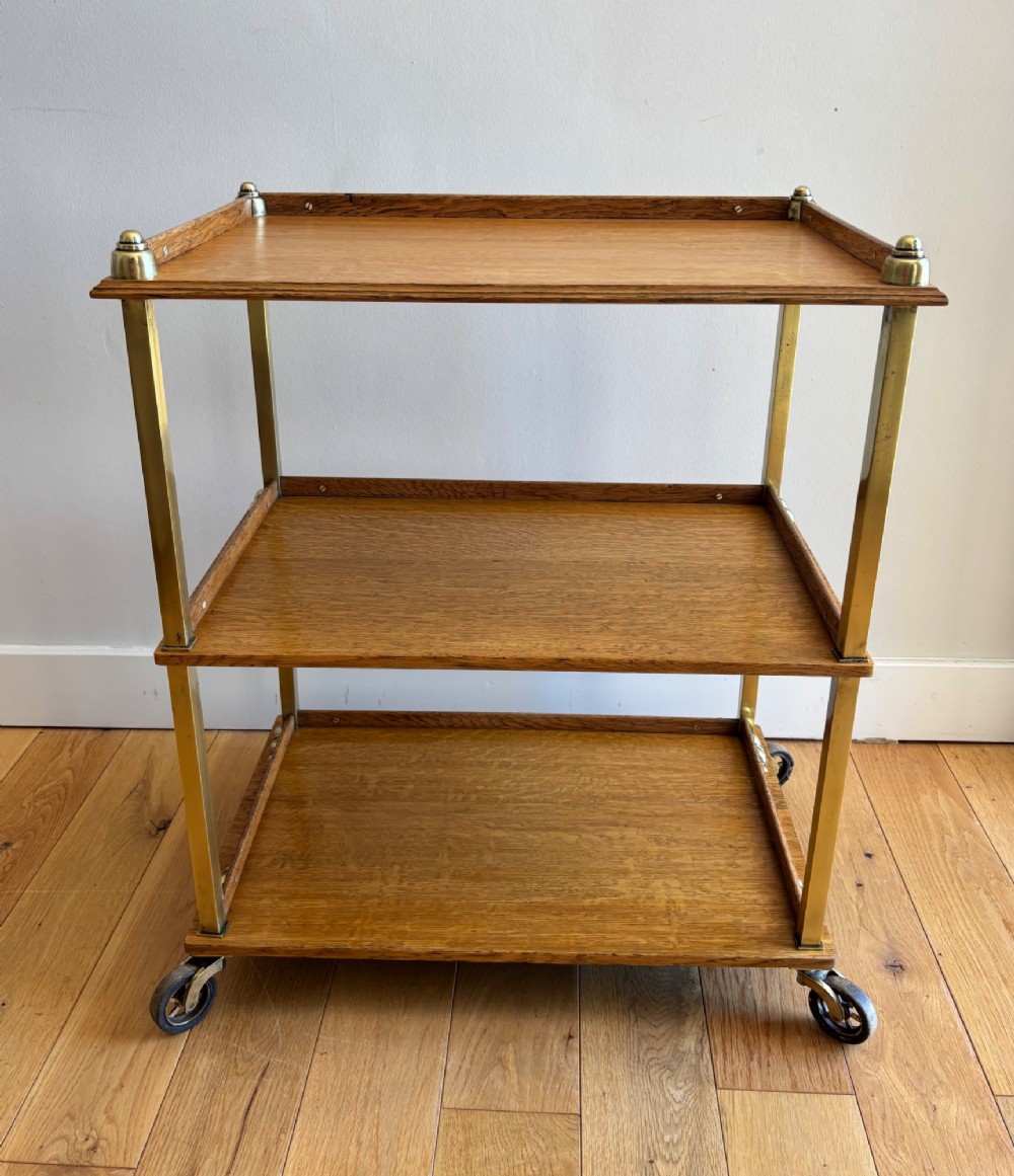 A late Victorian three-tier oak and brass etagere trolley with vertical brass supports and metal castors.