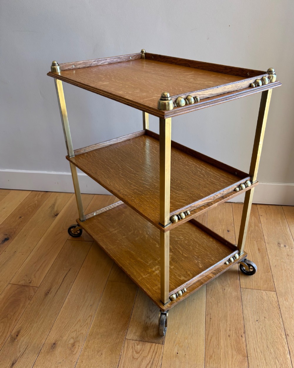 A late Victorian three-tier oak and brass etagere trolley with vertical brass supports and metal castors. View II