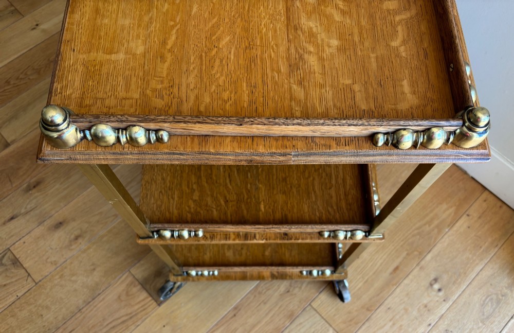 A late Victorian three-tier oak and brass etagere trolley with vertical brass supports and metal castors. View III