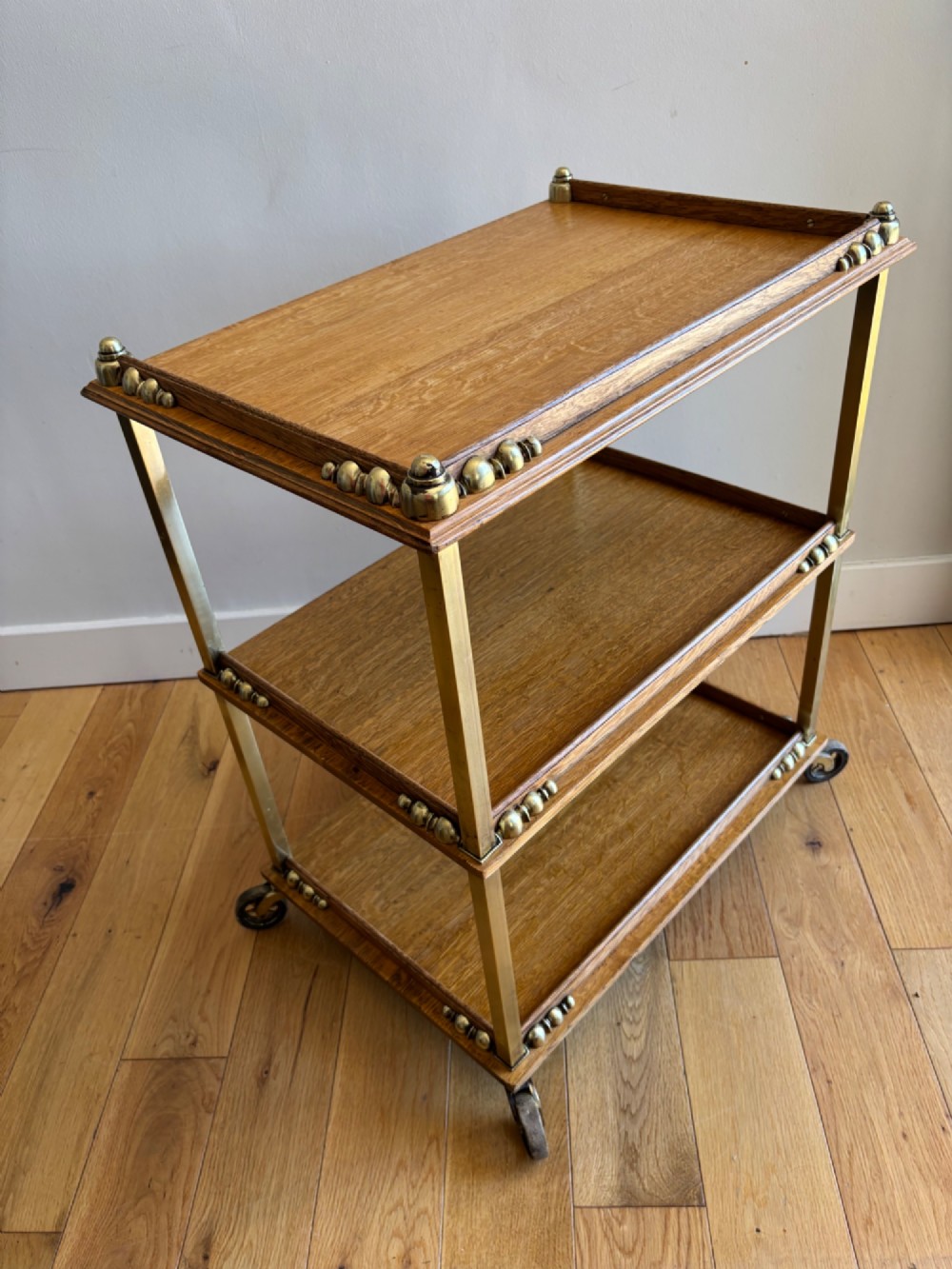 A late Victorian three-tier oak and brass etagere trolley with vertical brass supports and metal castors. View IV