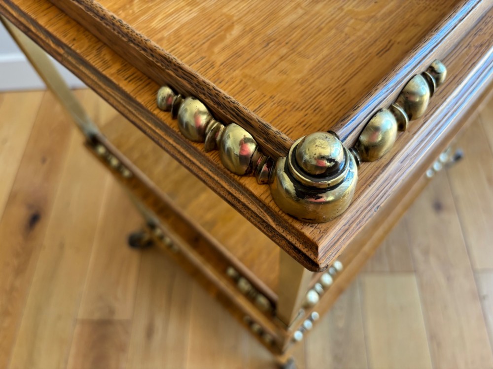 A late Victorian three-tier oak and brass etagere trolley with vertical brass supports and metal castors. View V