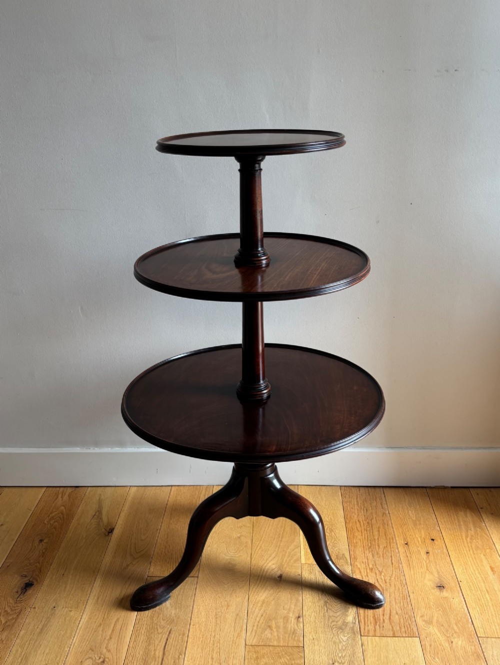 An early George III mahogany dumb waiter featuring three graduated circular trays on a turned central column supported by a tripod base with pad feet.