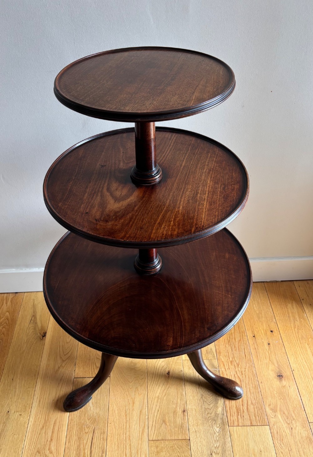 An early George III mahogany dumb waiter featuring three graduated circular trays on a turned central column supported by a tripod base with pad feet. View IV