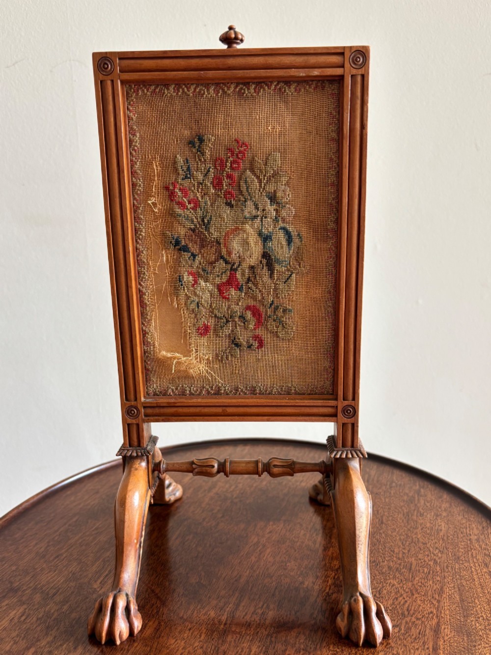 An antique Regency miniature mahogany fire screen featuring a carved frame, claw feet, and a central floral needlepoint textile panel.
