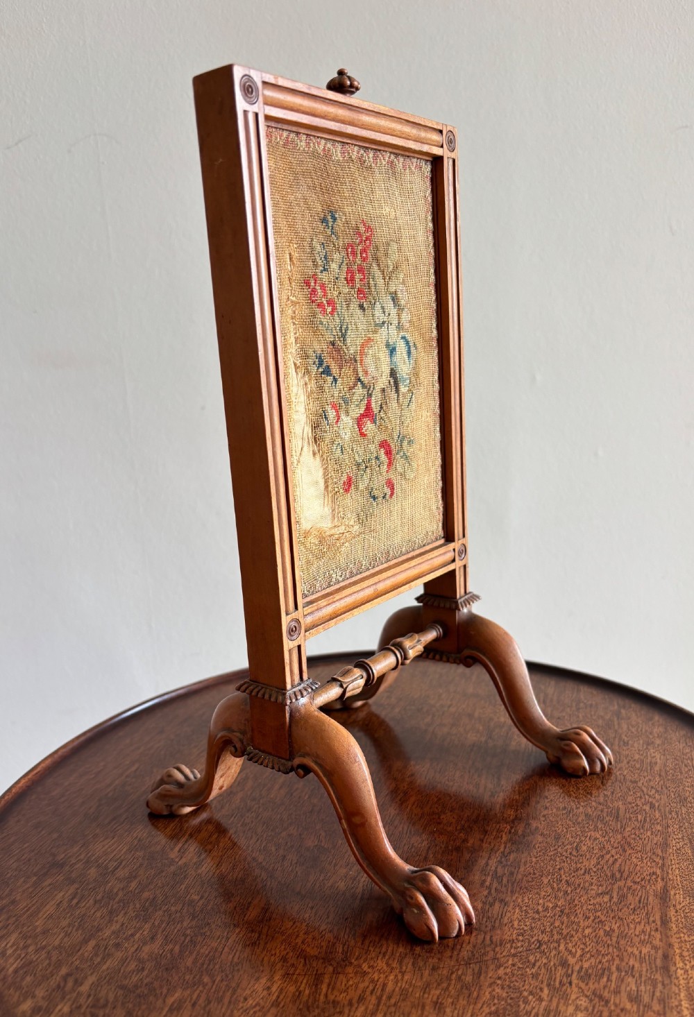 An antique Regency miniature mahogany fire screen featuring a carved frame, claw feet, and a central floral needlepoint textile panel. View II