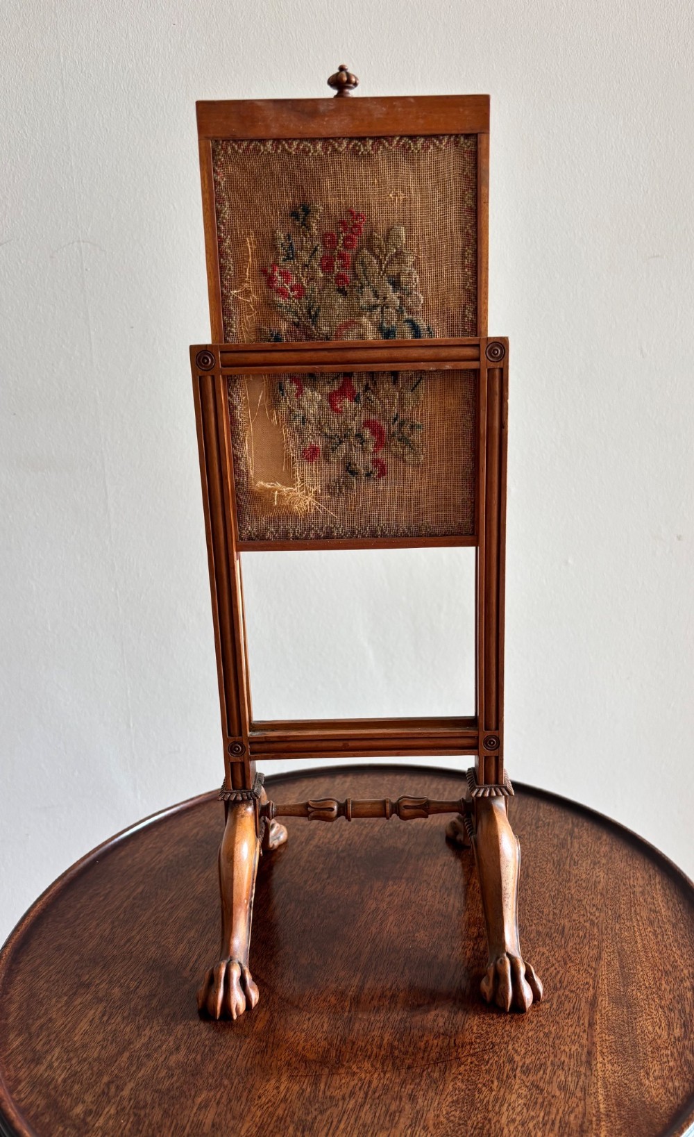 An antique Regency miniature mahogany fire screen featuring a carved frame, claw feet, and a central floral needlepoint textile panel. View III