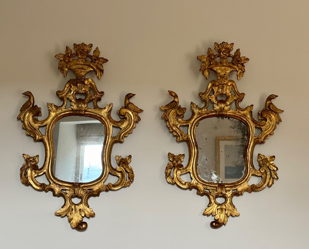 A pair of carved 18th century Venetian giltwood wall mirrors with crests featuring flower baskets and bird motifs flanking the frames.