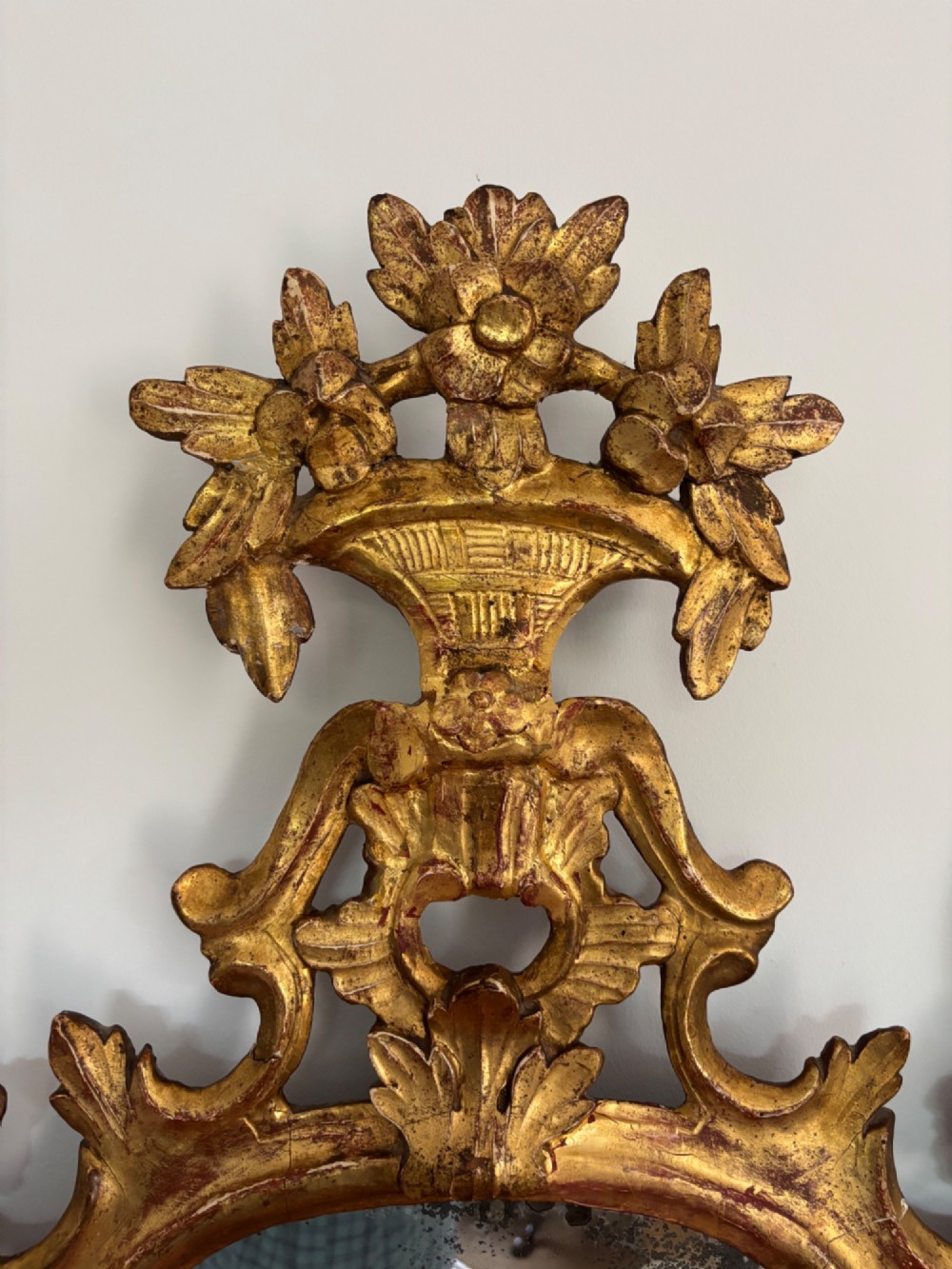 A pair of carved 18th century Venetian giltwood wall mirrors with crests featuring flower baskets and bird motifs flanking the frames. View II