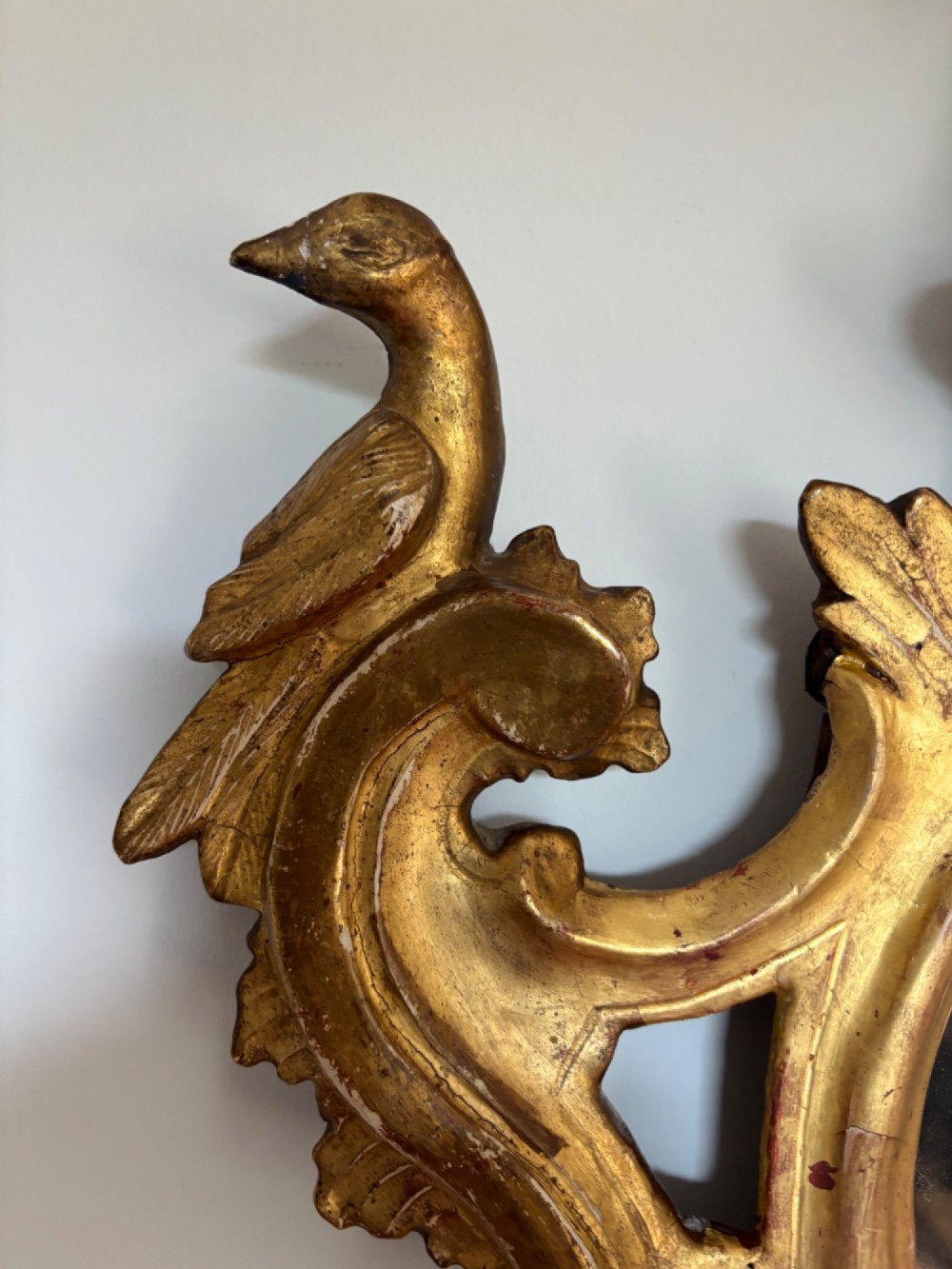 A pair of carved 18th century Venetian giltwood wall mirrors with crests featuring flower baskets and bird motifs flanking the frames. View IV