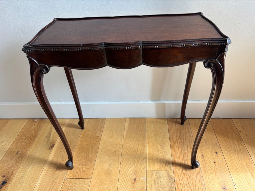 An Edwardian mahogany occasional table with a serpentine top, carved frieze, and slender cabriole legs.